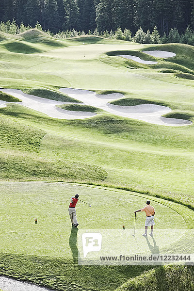Blick von oben auf zwei Golfspieler beim Abschlag auf einem Golfplatz.