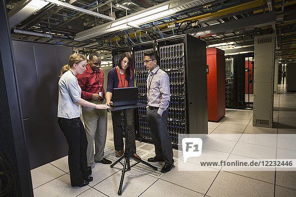 Mixed race group of technicians doing diagnostic tests on servers in a large server farm.