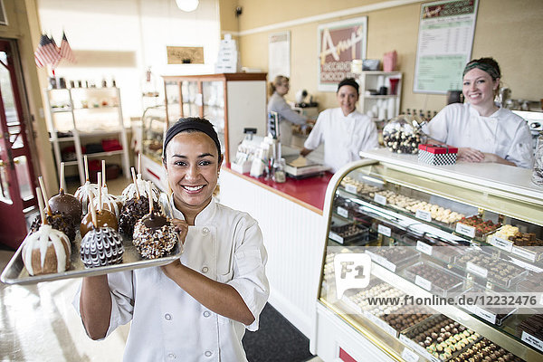 Hispanische Besitzerin eines Süßwarengeschäfts und ihr Personal im Hintergrund des Geschäfts.