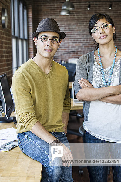 Asiatische Frau und hispanischer Mann zusammen an einem kreativen Büroarbeitsplatz.