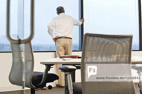 Geschäftsmann  der vor der nächsten Sitzung in einem Konferenzraum am Fenster steht.