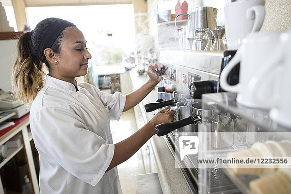 Hispanische Frau  die in einem Süßwarengeschäft an einer Espressomaschine arbeitet.