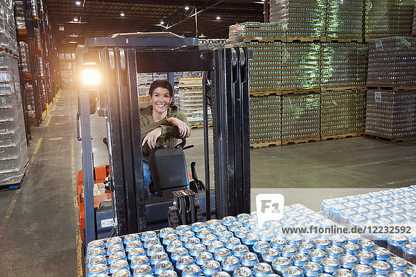 Portrait of a Caucasian female warehouse worker on a forklift in a warehouse full of pallets of flavoured water in cans.