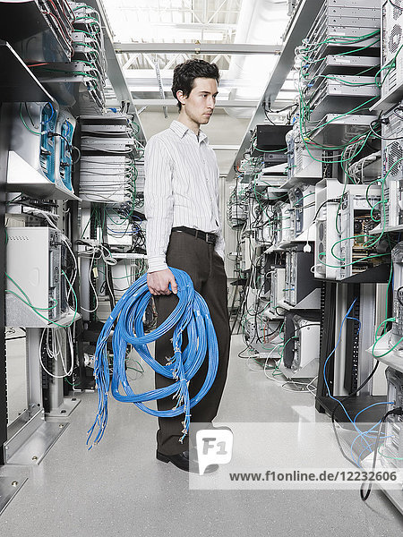 Male computer technician holding CAT 5 cables and standing in the aisle of a computer server farm.