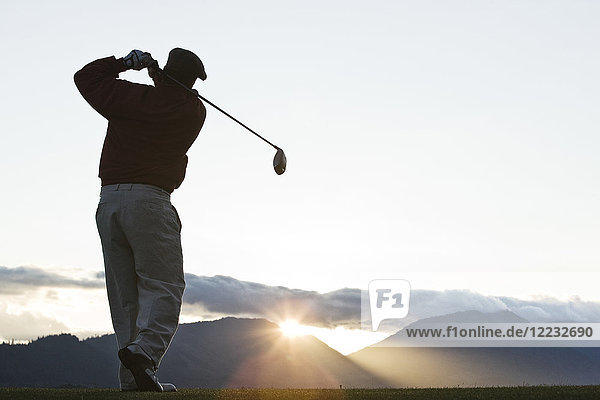 A golfer teeing off at sunrise.