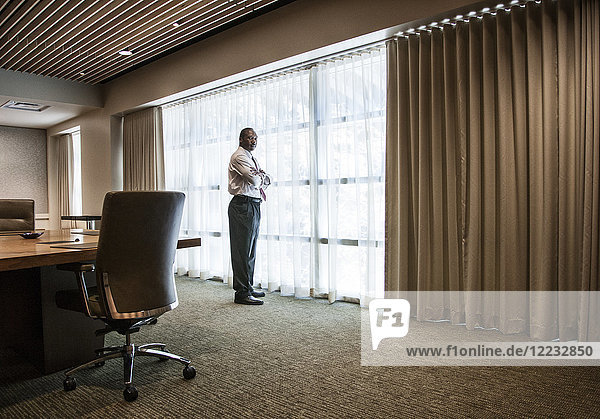 Black businessman standing at a window next to a large conference table.