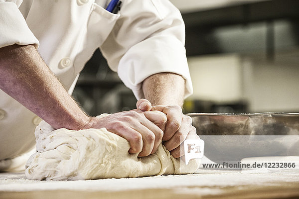 Die Hände eines Küchenchefs kneten Brotteig auf einer bemehlten Arbeitsplatte.