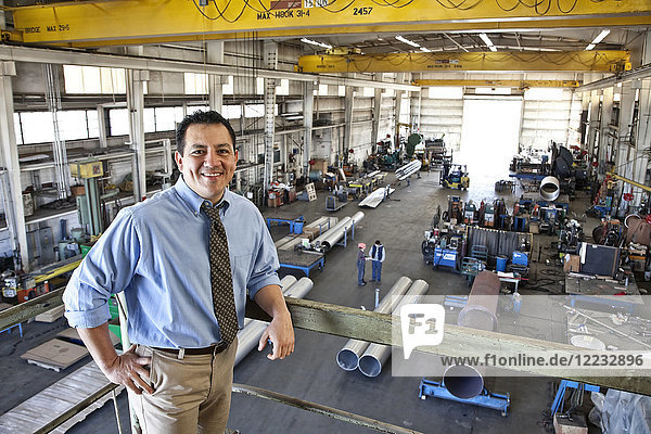 Hispanic man owner of a sheet metal factory standing above factory floor.