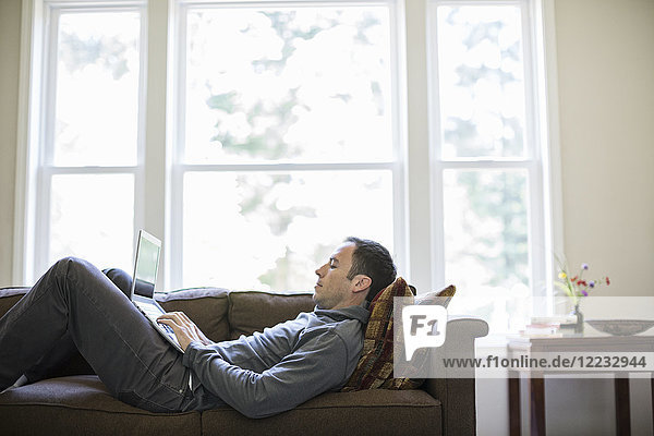 Kaukasischer Mann  der zu Hause auf dem Schoß arbeitet  während er auf einer Couch sitzt.
