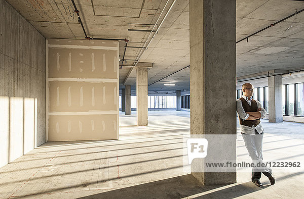 Asian businessman standing in a large empty raw office space.