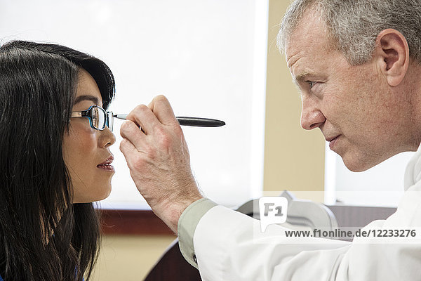 Caucasian male ophthalmologist working with an Asian woman who is purchasing a new pair of glasses.