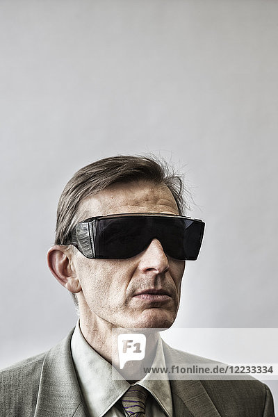 Studio portrait of Caucasian man actor wearing large sunglasses or protective eyeglasses with darkened lenses.