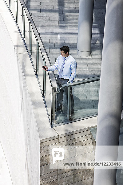 Caucasian businessman texting from a balcony on a large office building