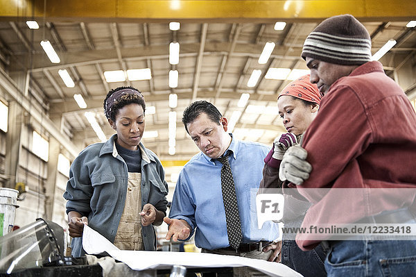 Mixed race team of workers and management people in a large sheet metal factory