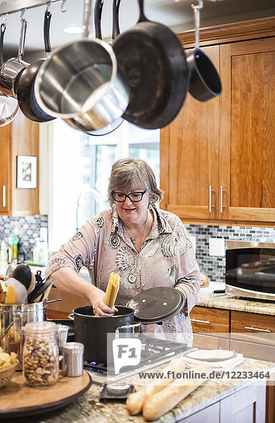 Ältere Frau  die überprüft  ob ein Topf mit Nudeln in der heimischen Küche richtig kocht.