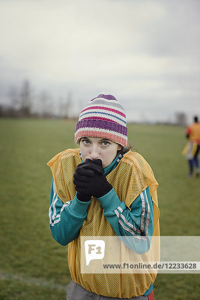 Caucasian woman blowing on her hands to stay warm at a sporting event in the winter.