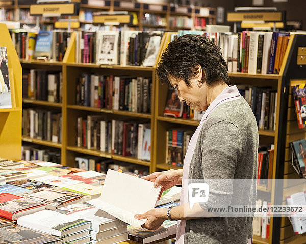 Asiatisch-amerikanische Frau blättert in einer Buchhandlung durch Bücher.