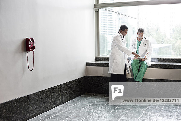 Caucasian and black men doctors conferring over a medical record in a hospital hallway.