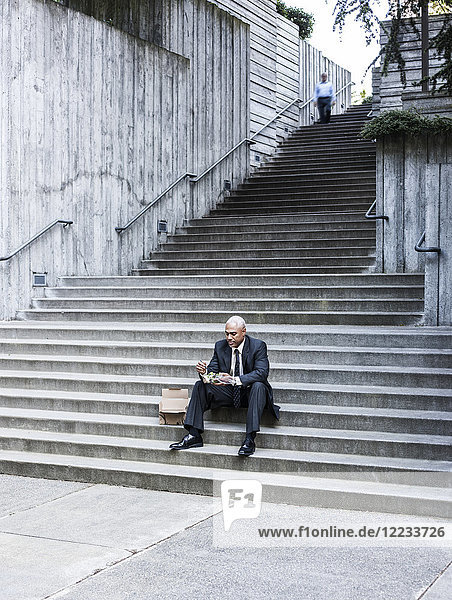 Schwarzer Geschäftsmann  der auf einer Treppenstufe sitzend eine Mittagspause macht.