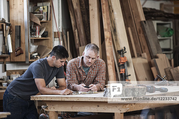 Team of two Caucasian men factory workers problem solving at a work station in a woodworking factory.
