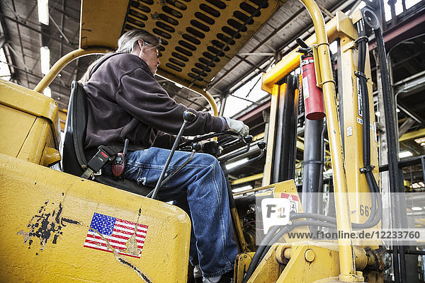 Caucasian man factory worker driving a fork lift in a sheet metal factory.