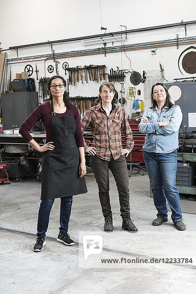 Three women standing in metal workshop  looking at camera.