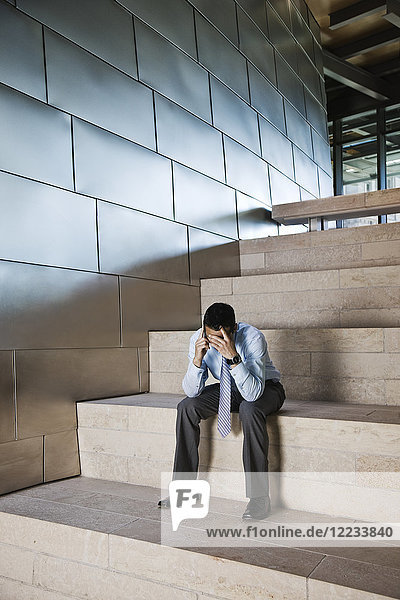 Businessman in a stressful situation while on a cell phone in the lobby of a large office building.