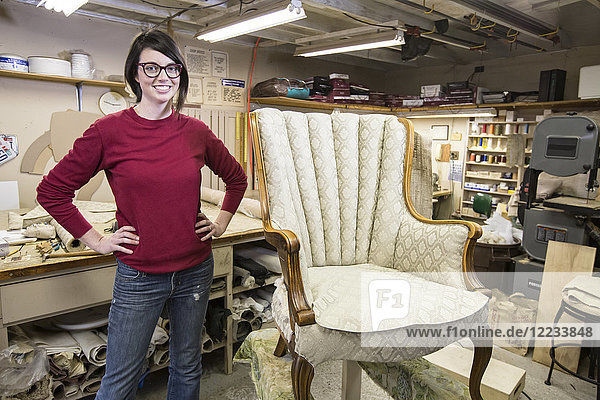 Porträt einer jungen kaukasischen Tapeziererin und eines Stuhls  an dem sie gerade arbeitet.