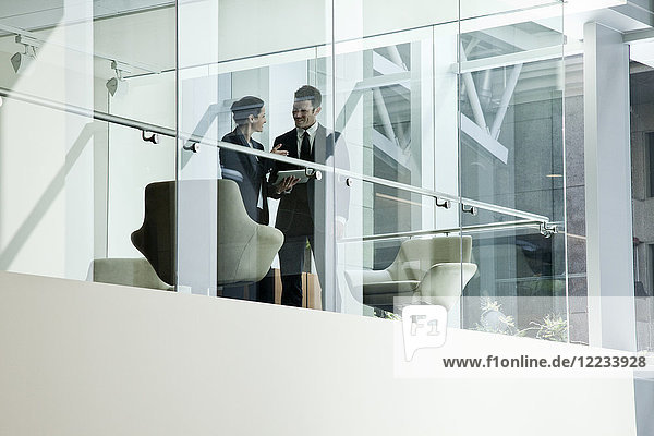 Businessman and woman standing behind a conference room window in large business centre.