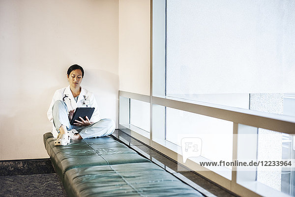 Asiatische Ärztin  die einen Notebook-Computer benutzt und einen Laborkittel und ein Stethoskop trägt.