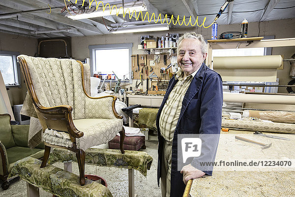 Caucasian senior male upholsterer working on a chair in his garage shop.