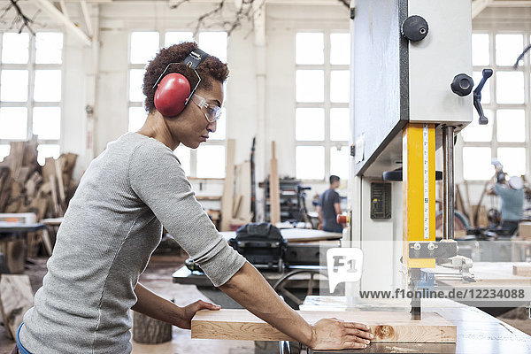 Black woman factory worker using a band saw to cut wood in a woodworking factory.