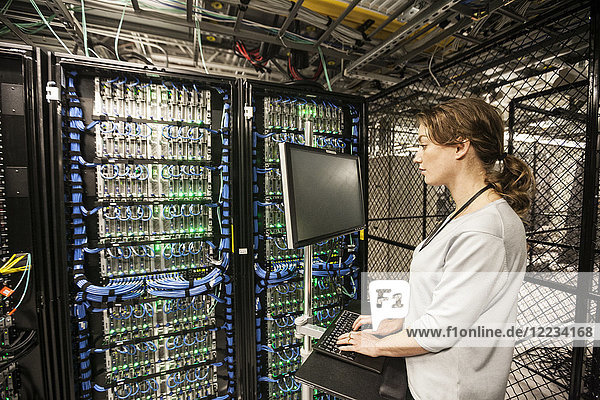 Caucasian woman technician doing diagnostic tests on computer servers in a server farm.