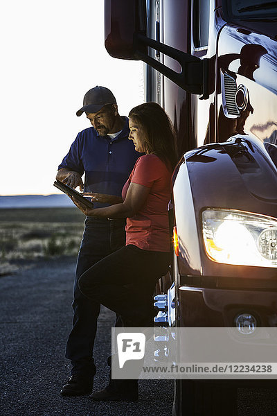 Ehemann und Ehefrau überprüfen nach Sonnenuntergang neben dem Fahrerhaus ihres Lastwagens das Logbuch ihres Notebook-Computers.