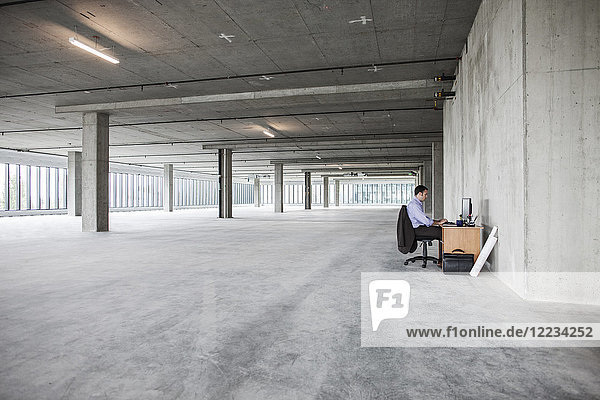 Businessman sitting at a small desk in a large empty raw office space.