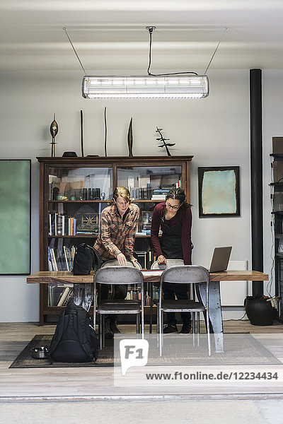 Zwei Frauen versammelten sich im Bürobereich einer Metallwerkstatt um einen Tisch und betrachteten technische Entwürfe.