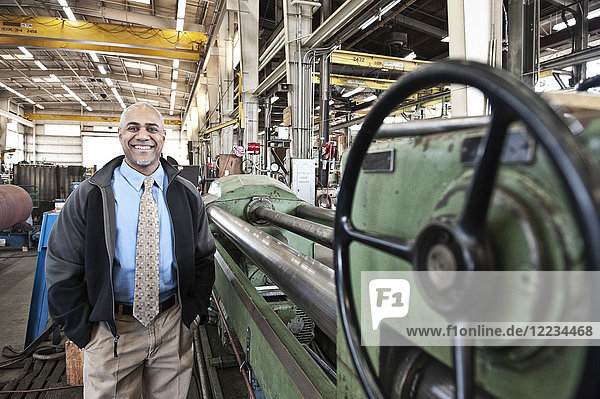 A black man owner of a sheet metal factory standing on the floor of the factory.