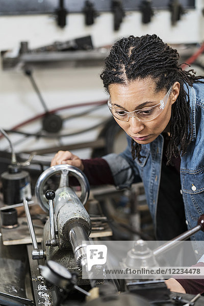 Woman wearing safety glasses standing in a metal workshop  working at a machine.