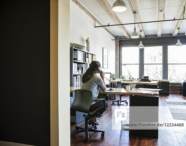 Asiatische Frau  die an ihrem Schreibtisch in einem kreativen Büro arbeitet.