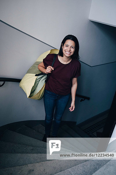 High angle portrait of smiling woman carrying bag while standing on steps