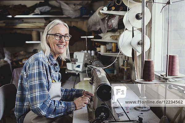Porträt des lächelnden Besitzers mit Nähmaschine in der Werkstatt