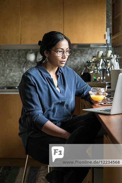 Businesswoman holding juice while using laptop in home office