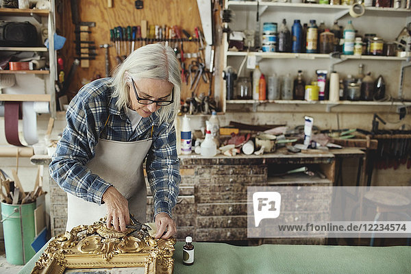 Senior Handwerker arbeitet über geschnitztem Holzrahmen am Tisch in der Werkstatt