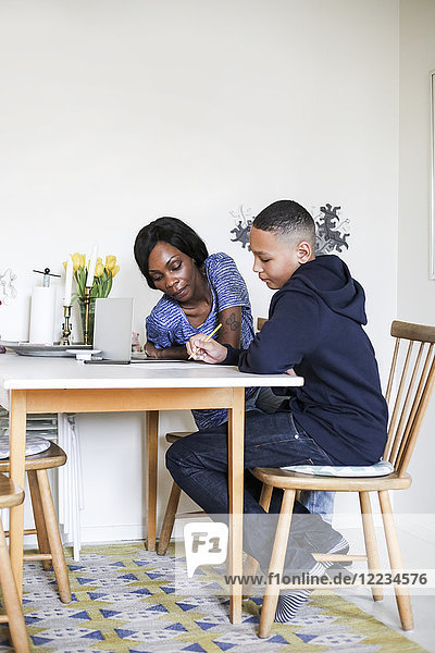 Mother helping son doing homework at dining table