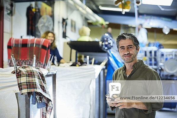 Porträt eines lächelnden  reifen  männlichen Arbeiters mit Handy in der Werkstatt