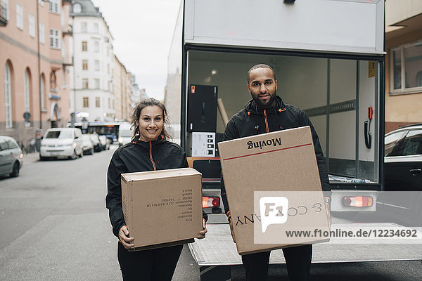 Porträt von Arbeiterinnen und Arbeitern die Kisten tragen während sie gegen den Lieferwagen in der Stadt stehen.