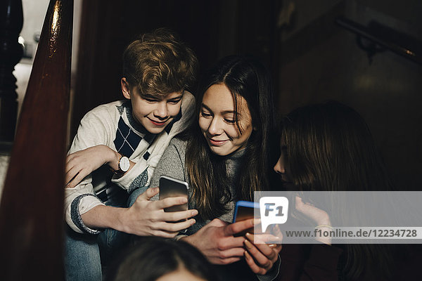 Lächelnder Teenager der weiblichen Freunden das Handy zeigt während er auf einer Treppe sitzt.
