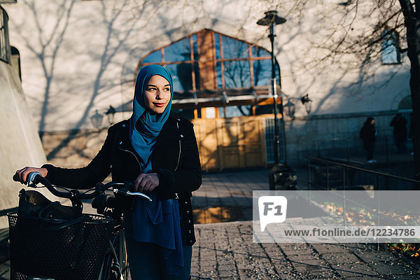 Selbstbewusste junge Frau die mit dem Fahrrad auf einem Fußweg gegen das Bauen in der Stadt geht.