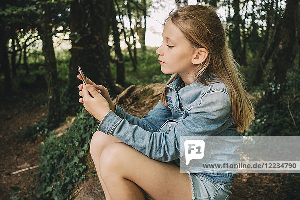 Side view of blond girl using smart phone in forest