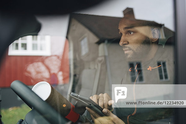 Man holding digital tablet seen through windshield of delivery van